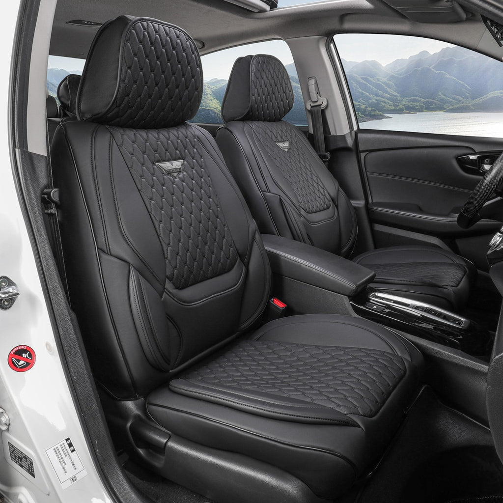 Black car seat covers installed on the front seats of a vehicle, featuring quilted diamond stitching and a small wing logo on the backrests, shown from the open driver's side door with a scenic mountain lake view outside.