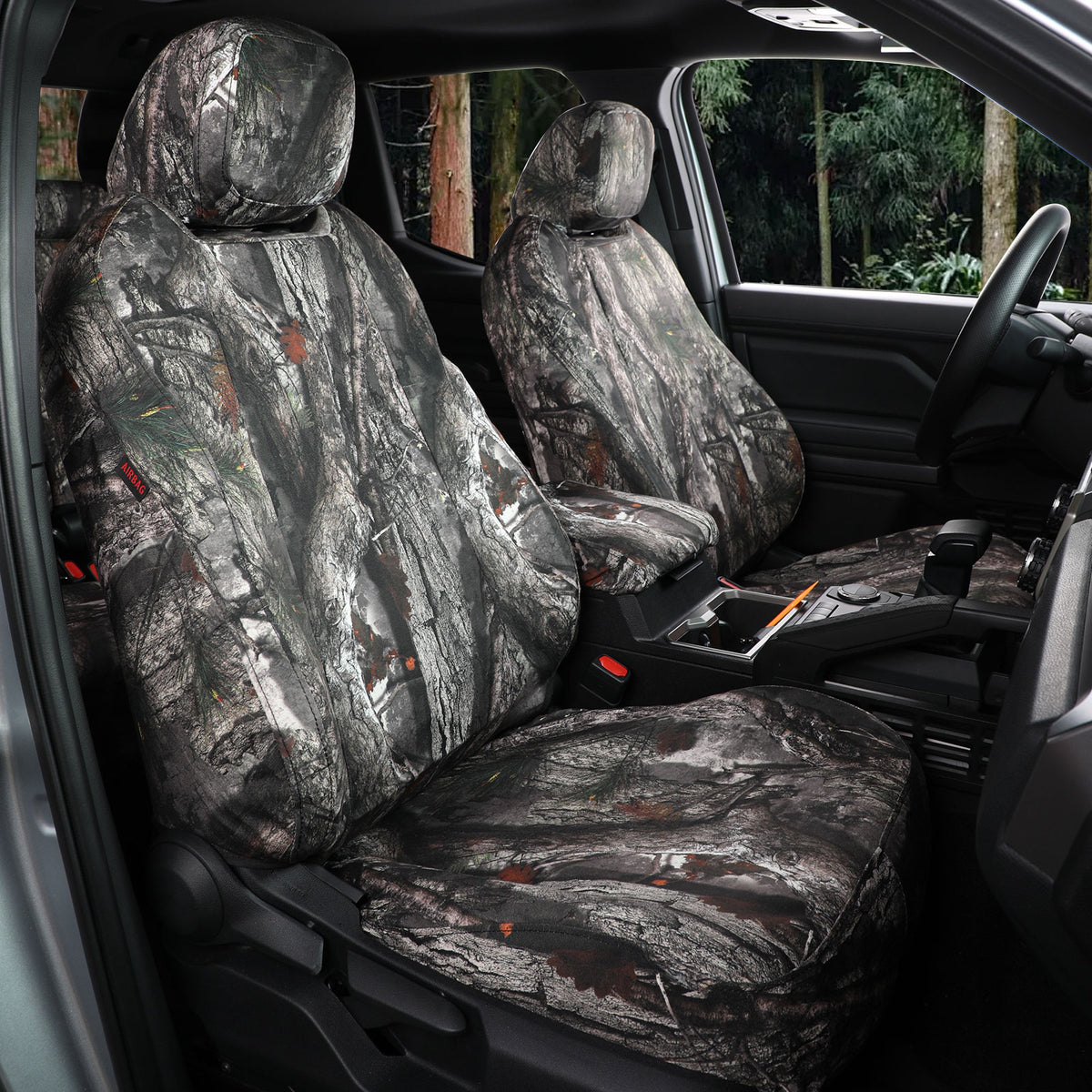 Front car seat covers with a realistic woodland camouflage pattern installed inside a vehicle cabin, showing the driver's side and center console area.