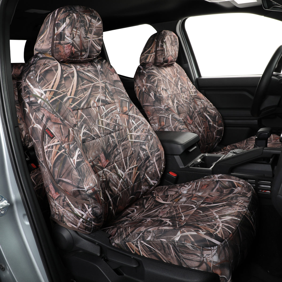 A pair of car seat covers with a brown and beige marsh grass camouflage pattern installed on the front seats of a vehicle interior.