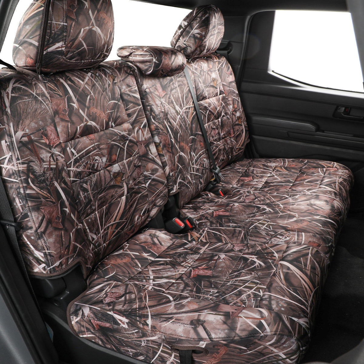 A set of car rear seat covers with a brown and beige marsh grass camouflage pattern installed on the back seats of a vehicle.