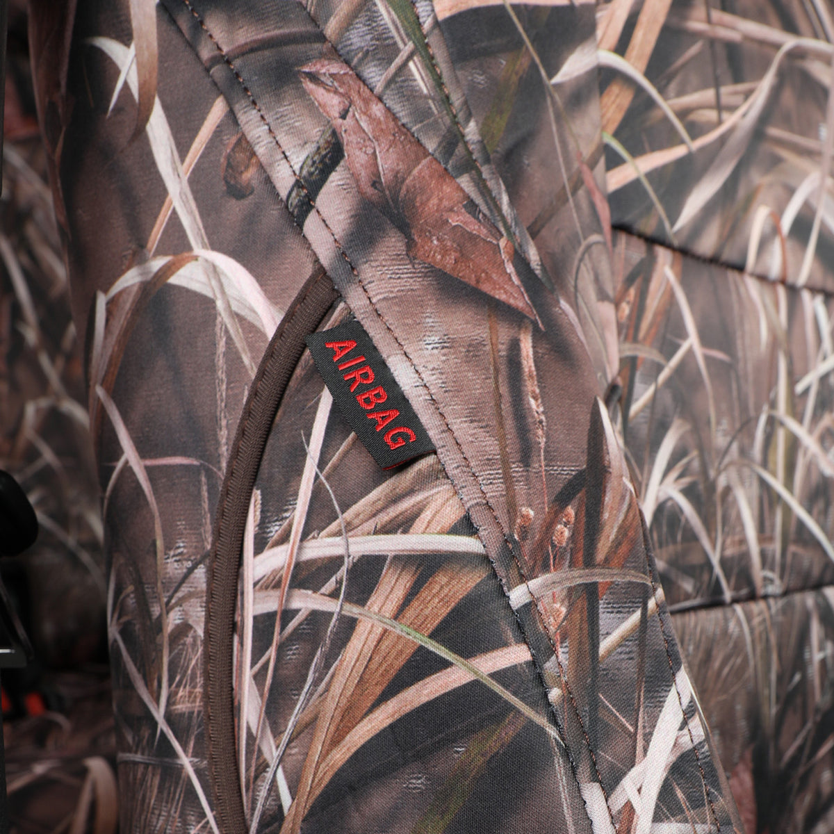 Close-up of a camouflage-patterned inflatable airbag with a small black label reading 'AIRBAG' in red text, showing a marsh grass and leaf print.