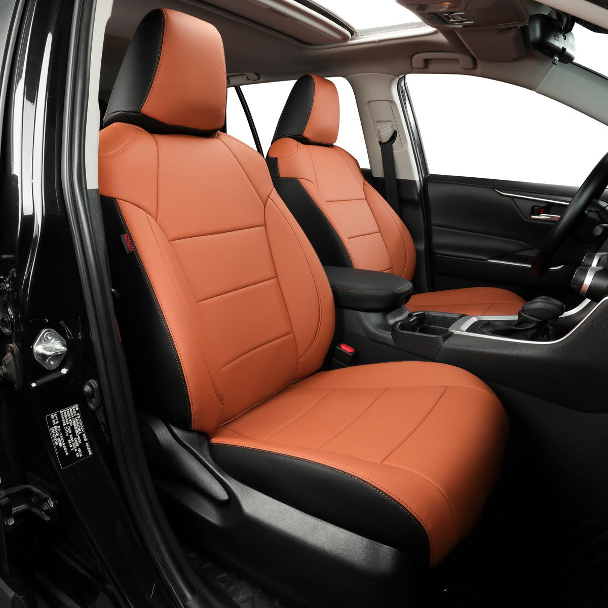 Brown and black car seat covers installed on the front seats of a vehicle interior, shown from the open driver's side door.