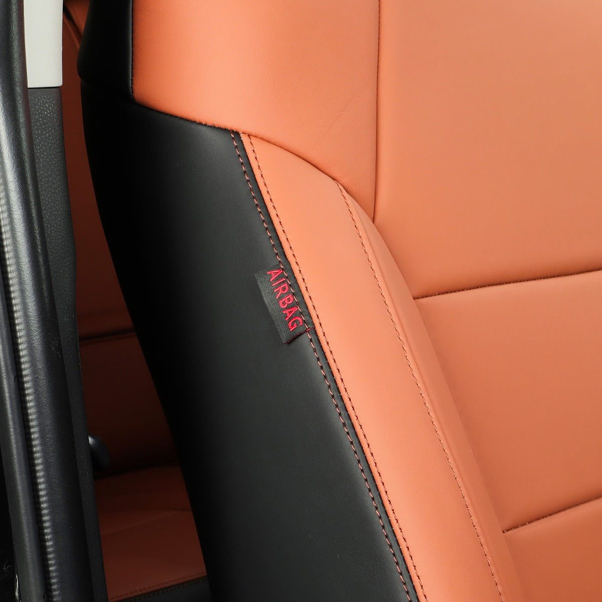 Close-up of a car seat with Brown and black leather upholstery, showing a small red AIRBAG label on the side bolster.