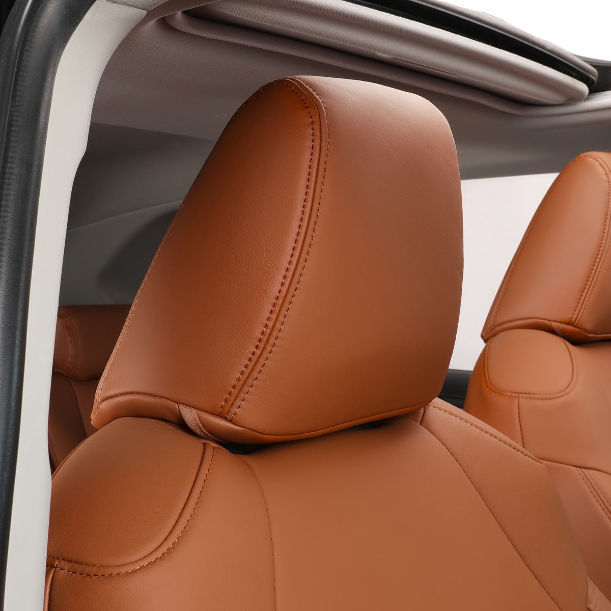 A close-up of a tan leather car seat headrest and backrest with visible stitching, set inside a vehicle interior.