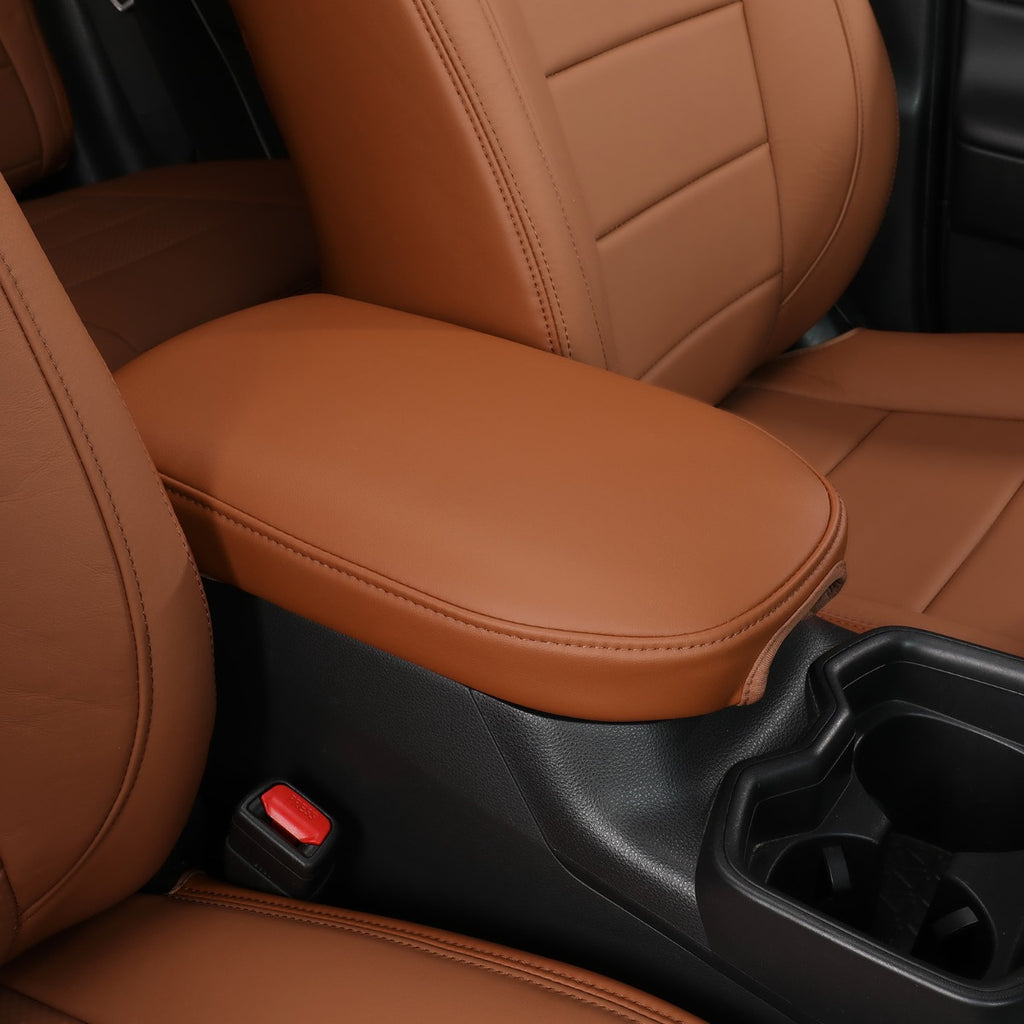 A close-up of a car interior showing tan leather seat covers on the front seats and center console armrest, alongside a black center console and cup holders.