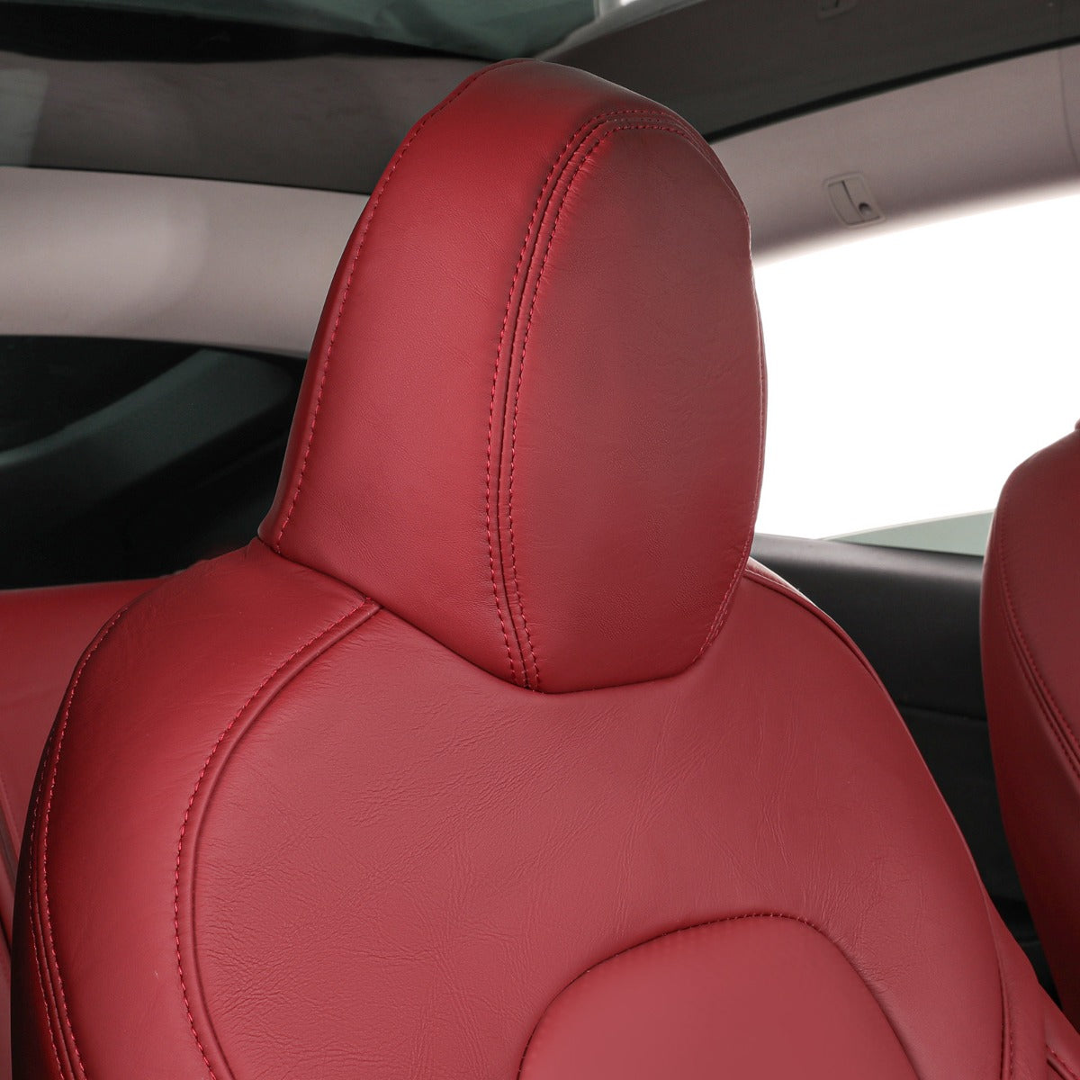 A close-up of a car seat with a matching headrest in burgundy leather, showing the interior car cabin and part of another seat.