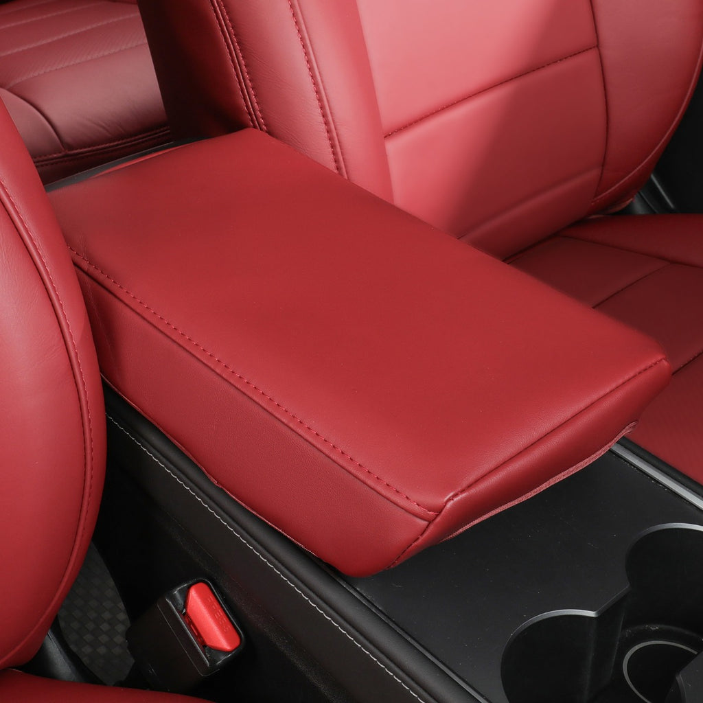 A close-up of a car interior showing a burgundy leather or faux-leather center console armrest between red seats, with part of the black center console and cup holders visible below.