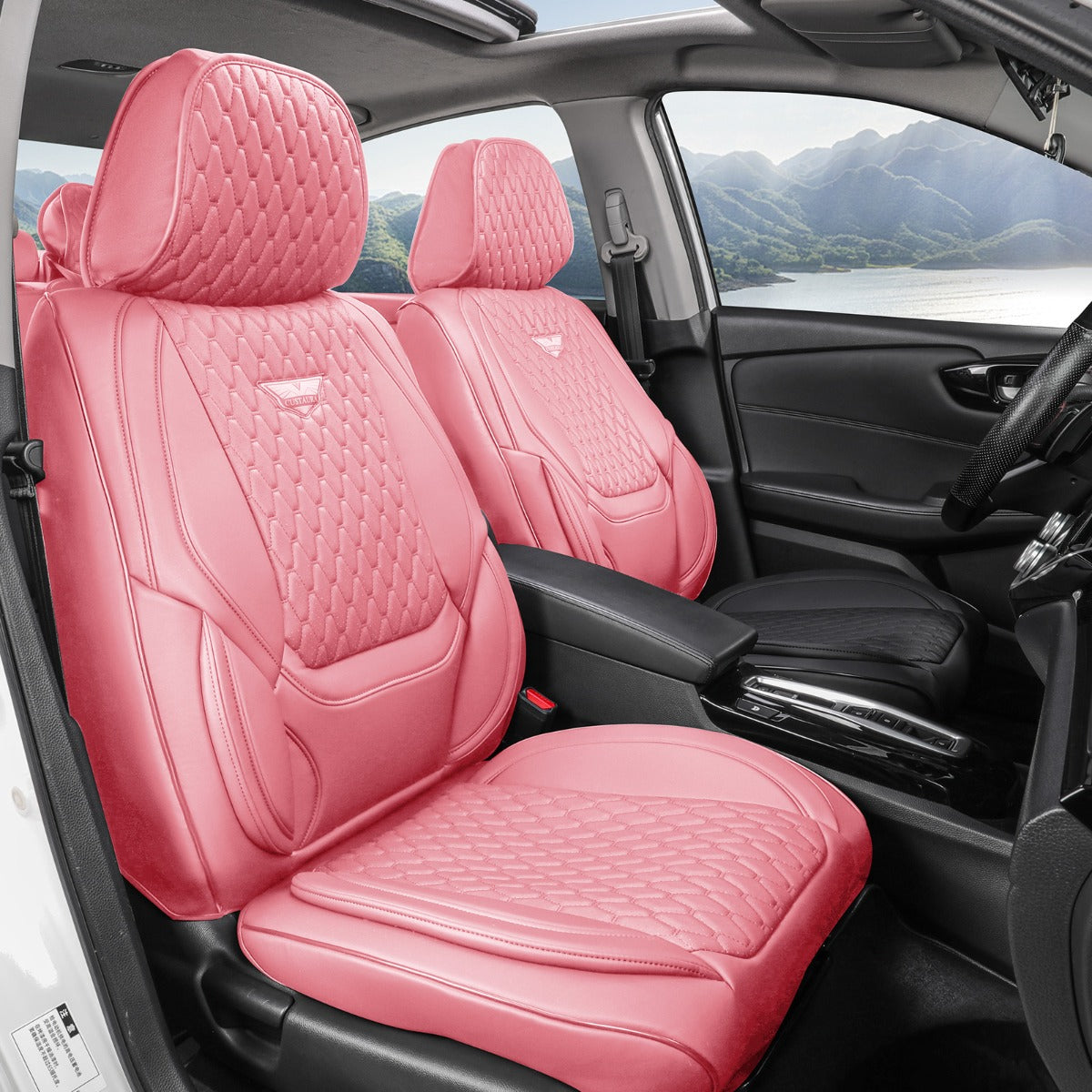 A pair of pink car seat covers installed on the front seats of a black car interior, with a scenic mountain lake view visible through the windows.