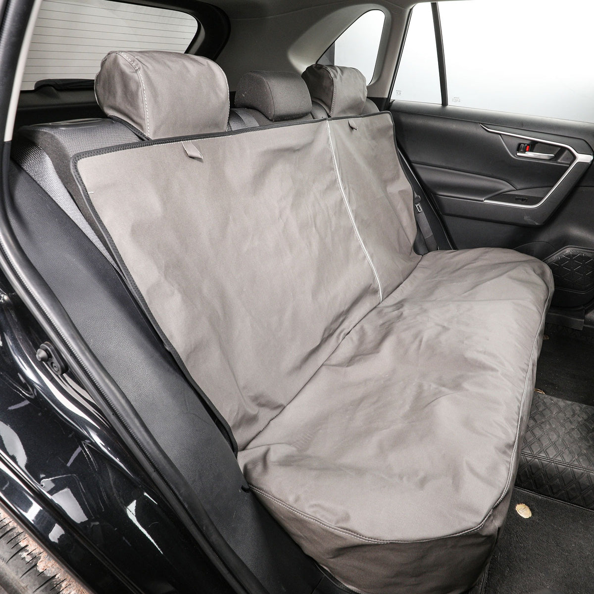A gray car seat cover installed on the back seat of a vehicle, shown from the rear door area with the seat headrests and car interior visible.