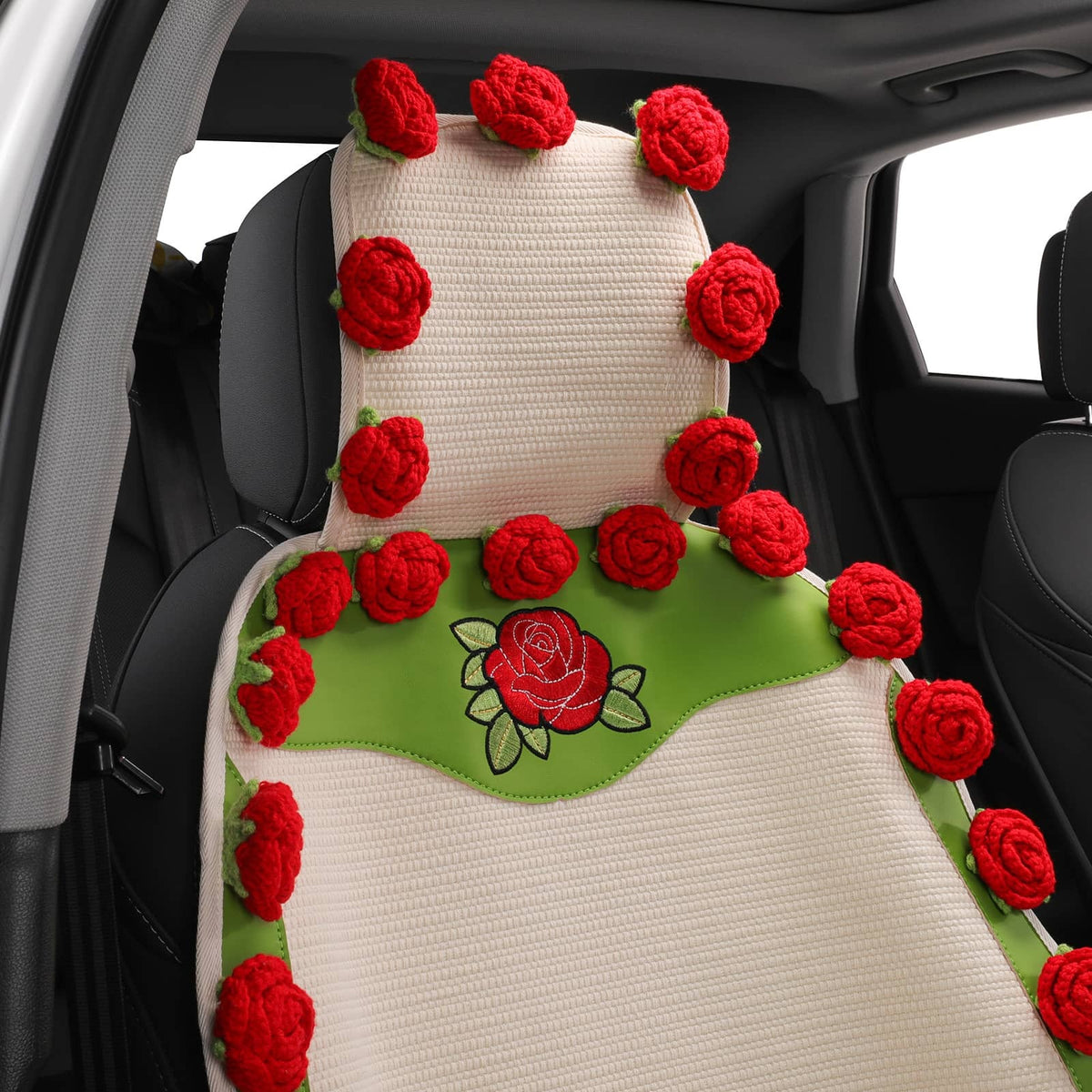 A car seat cover with a textured cream mesh body, green fabric trim, embroidered red roses, and red crocheted rose accents, shown installed on a car seat inside a vehicle.
