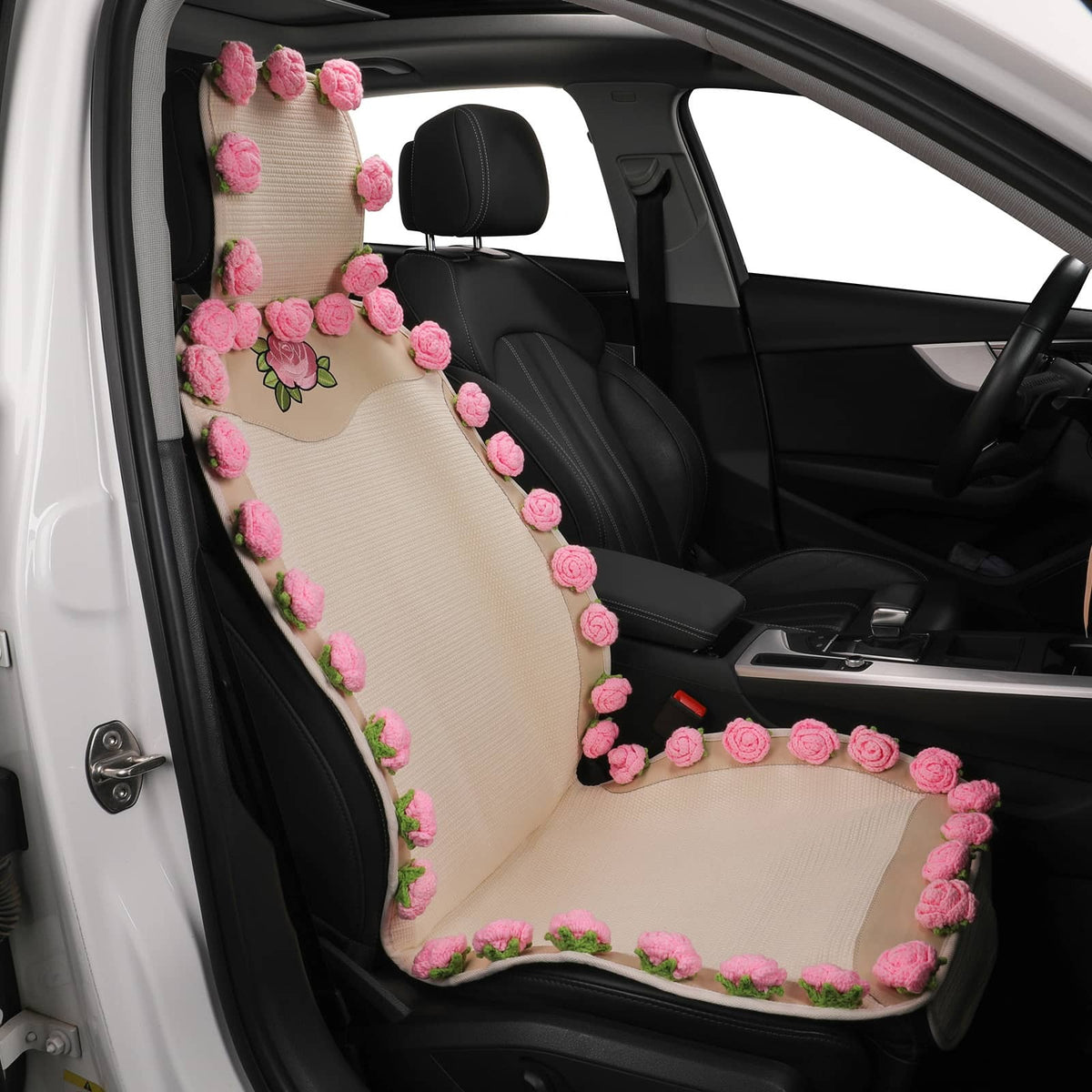 A beige car seat cover on the front passenger seat of a black car, decorated with pink 3D roses and green leaves along the edges.