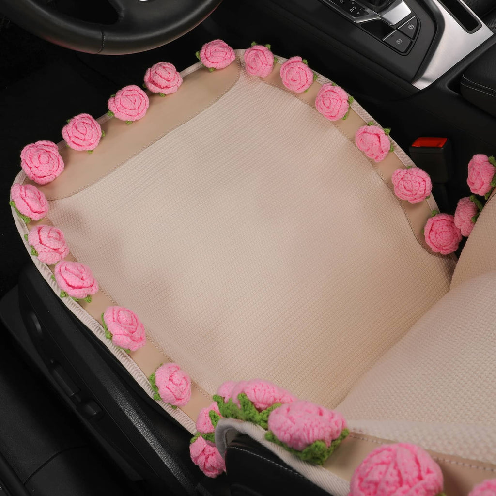 A beige car seat pad with pink crocheted roses and green leaves, shown installed on a car seat.